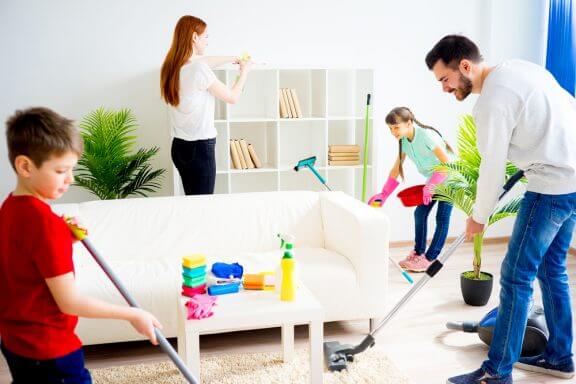 Familie gør rent i stuen sammen. Mor tørrer hylder af, far og søn støvsuger.