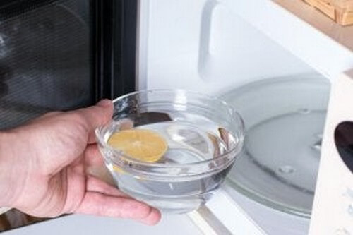 Person rengører mikroovn med vand og citron 