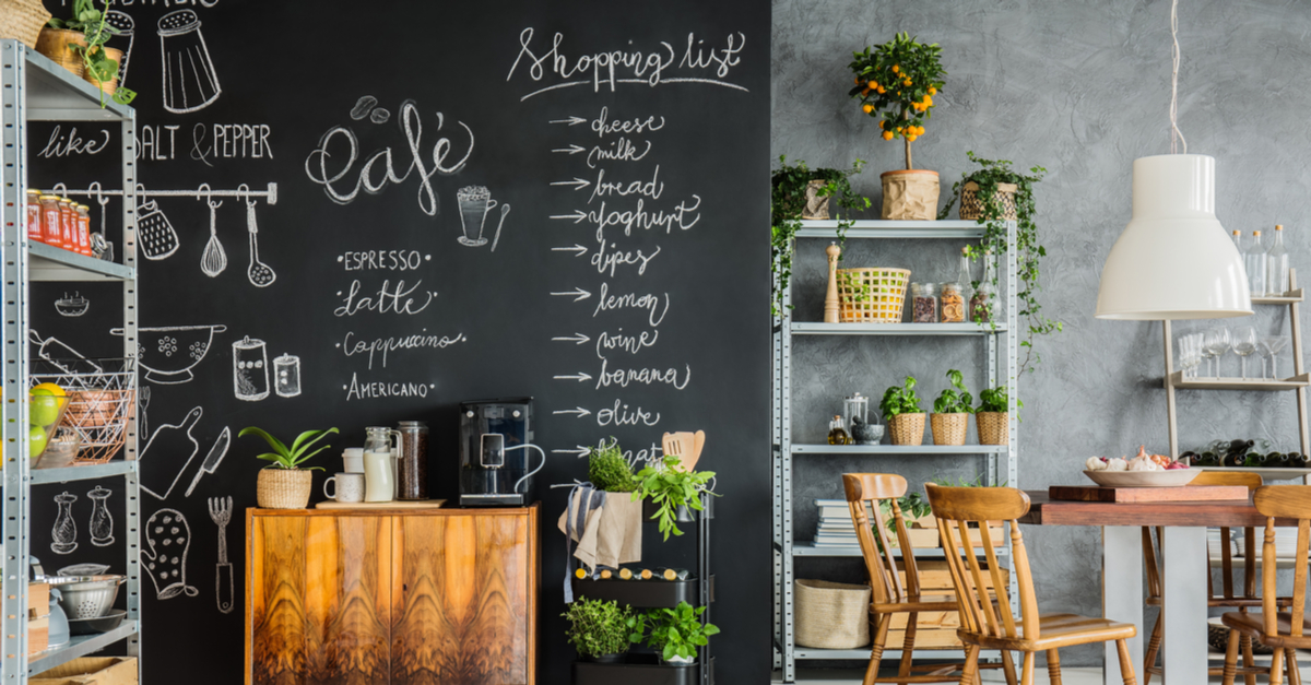 A kitchen with indulstrial shelves, wooden furnitue, plants, and a chalkboard wall.