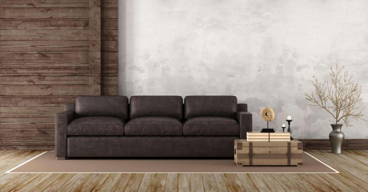 Salón rústico con sofá de piel oscuro y pared y suelo de madera