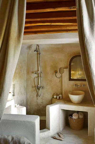 A white stone bathroom with exposed wooden beams on the cieling.