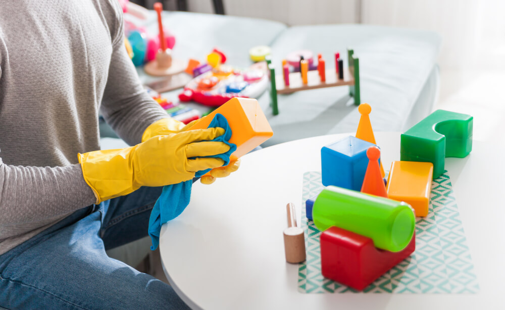 A man wearing rubber gloves and washing plastic toys with a wash cloth.