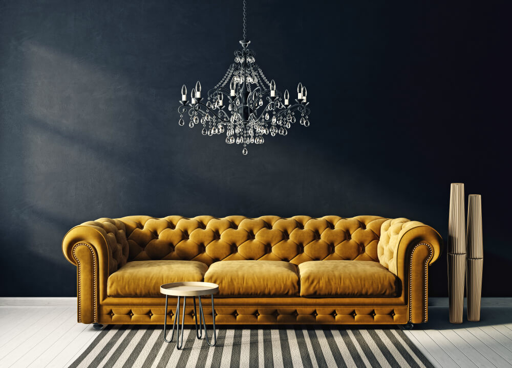 A mustard colored Chesterfield sofa against a black wall.