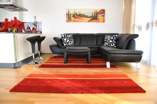 Salotto con divano in pelle nera e tappeto colore arancione rosso.