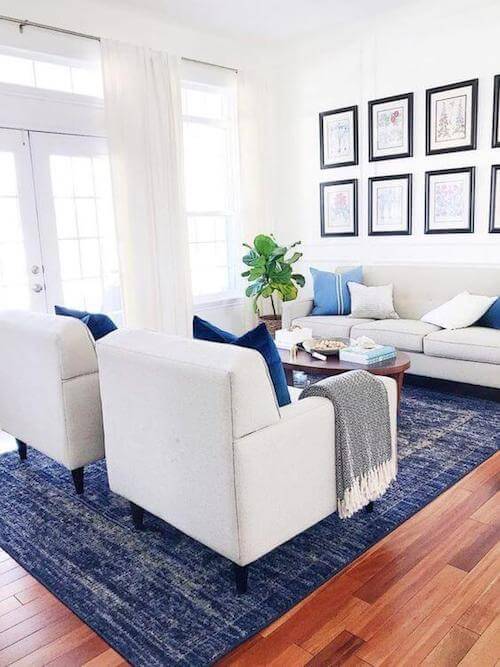 Salotto con tappeto cuscini blu divano poltrone e tende bianche