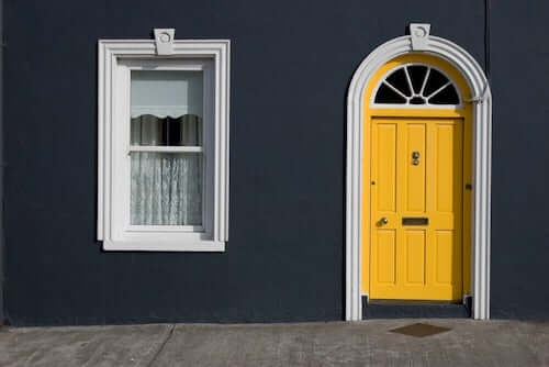 Casa con facciata color nero, porta gialla e finestra bianca.