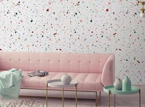 Salone con divano rosa e pareti con texture graniglia.