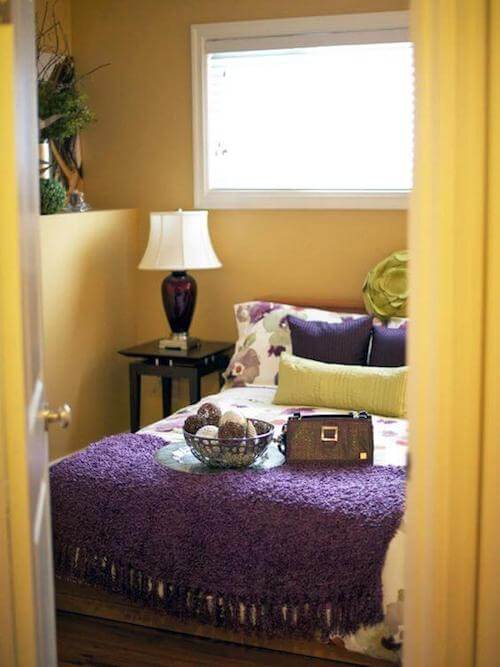 Camera da letto gialla con coperta e cuscini color viola.