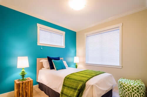 Parete della camera da letto in blu verdastro. Coperta, lampade e pouf di colore verde.