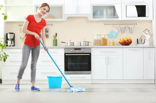 Donna che pulisce il pavimento della cucina.