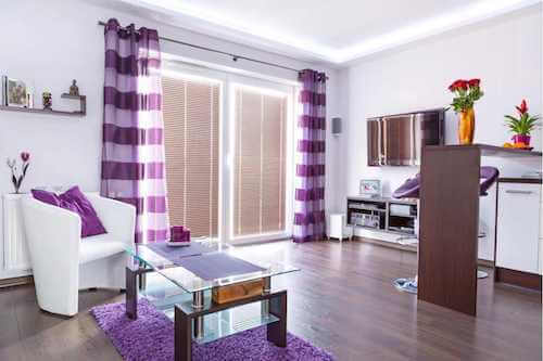 Soggiorno con tende, tappeto, cuscino e complementi d'arredo color lilla.