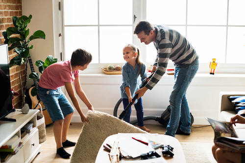 Padre e figli che puliscono il soggiorno. Padre e figli che passano l'aspirapolvere in soggiorno.