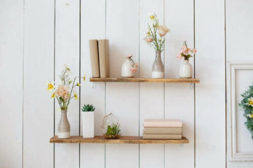 Beyaz duvarda üstünde çiçek ve kitap olan raf