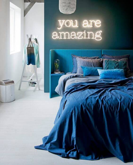 Mavi tonlarında yatak odası ve neon yazı