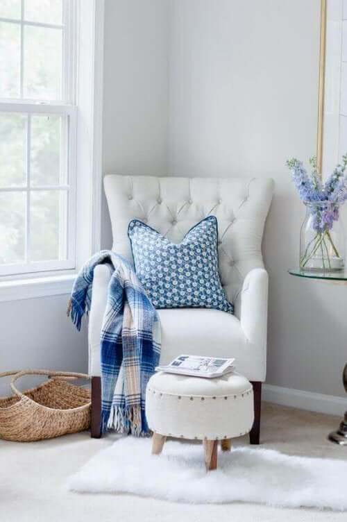 Beyaz koltuk ve mavi dekoratif ürünlerin olduğu okuma köşesi