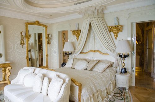 White and gold Victorian style bedroom with a canopy and gilded mirror