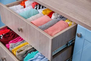 A picture showing a dresser with a couple drawers open, full of clothing.