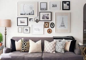 A living room shown with a big couch with lots of pillows, and lots of frames of different shapes and sizes on the wall above it.