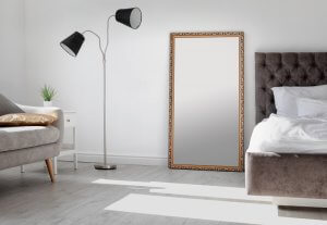 A picture shows a living room with grey, hard wood floors with a mirror anchored to the wall.