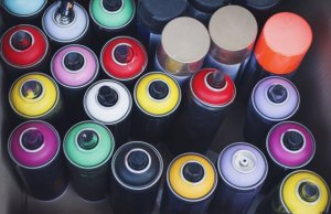 A bunch of spray paint cans with various top colors are bundled up in a small space, pictured from above.