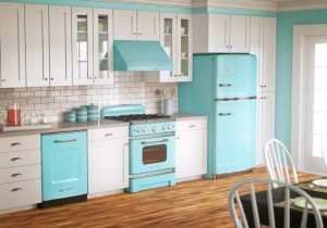 A kitchen with a wood floor and vintage metal appliances is seen at an angle that shows cabinets, dishwasher, stove, and fridge (which are painted sky blue).