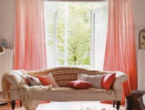 Pink curtains spread apart in front of open windows looking out onto a green outdoor space.