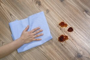 A person cleaning up a mess on a wooden floor with a rag, which is important if you want to care for wood furniture.