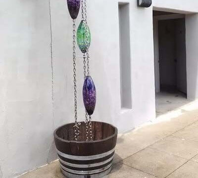 A rain chain with colored pieces of crystal and a wooden bucket