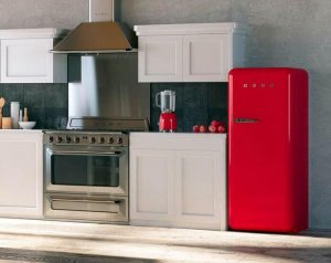 A kitchen with wooden floors at an angle that we can see its metal stove, white cabinets, and red refrigerator, painted with stainless steel paint.