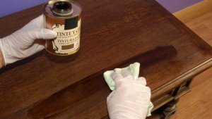 A person with latex gloves on their hands is wiping their furniture with wood wax.
