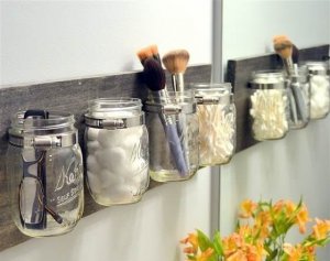 Mason jars are holding various bathroom accessories, fixed to a wooden board.