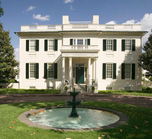 A grand, white colonial house with a wrap-around driveway.