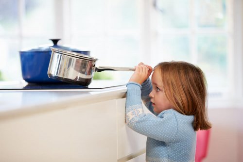 A child pulling a pot from the stove.