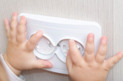 A child's hands on a covered electrical outlet.