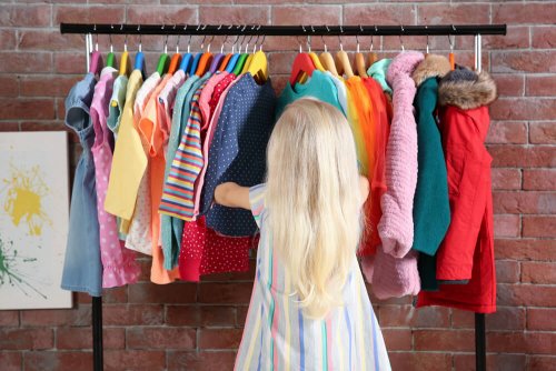 A little person looking through hanging garments at their walk-in closet..