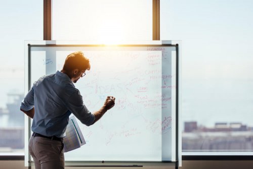 A man writing on a glass bulletin board.