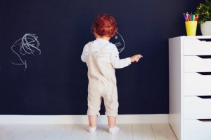 A toddler drawing on a chalkboard wall.
