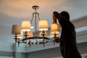 A man changing the bulbs in a chandelier.