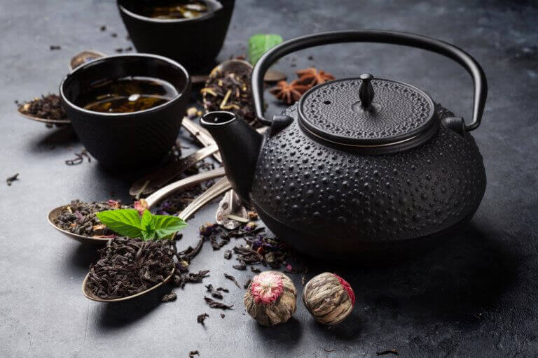 A black ceramic teapot with dried leaves and spices