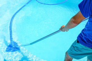 A man is using a manual pool cleaner.