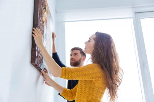 A couple hanging a painting on the wall.