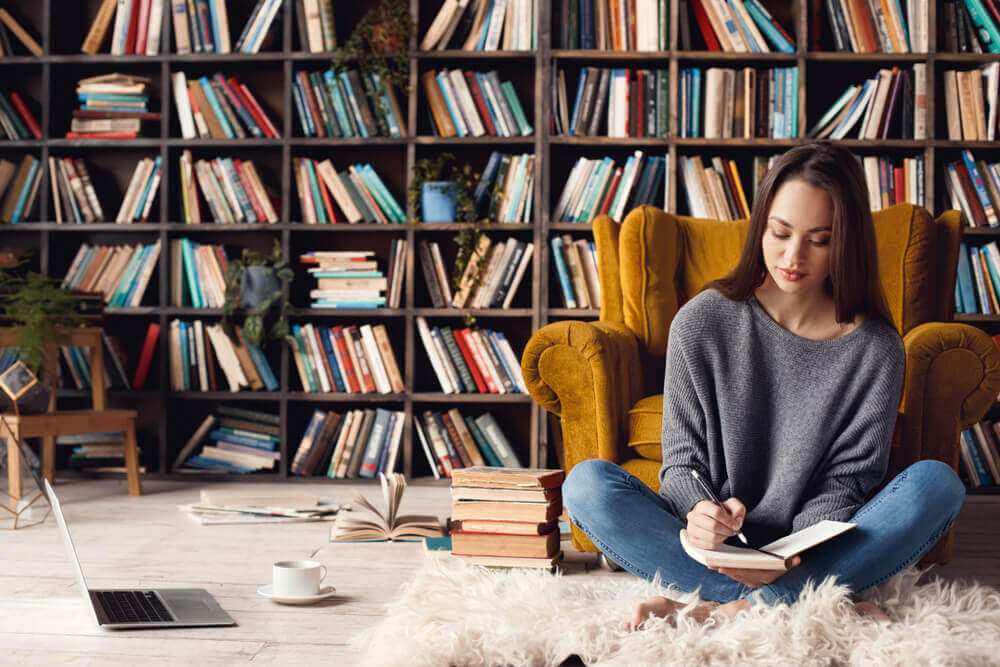 A woman sitting on the floor reading in a room with lots of bookshelves.