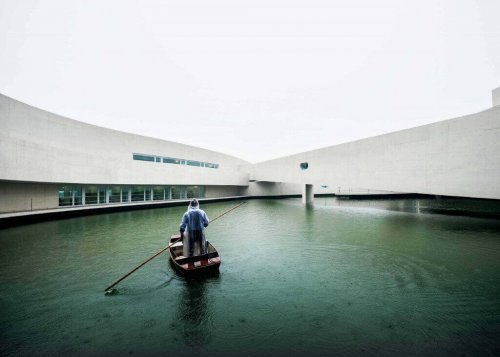 A man standing in a rowboat in water between wings of a building