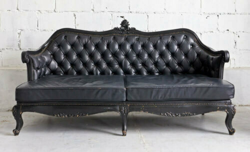 Black Victorian style sofa against a white wall.
