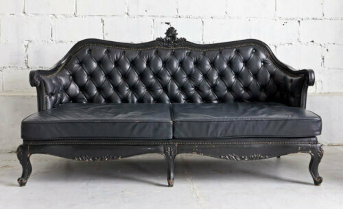 Black Victorian style sofa against a white wall.