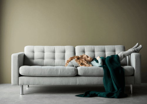 A little girl lying down on a gray sofa.