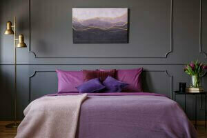 A bed with violet sheets and gray wall