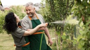 A man and woman watering plants with a hose.