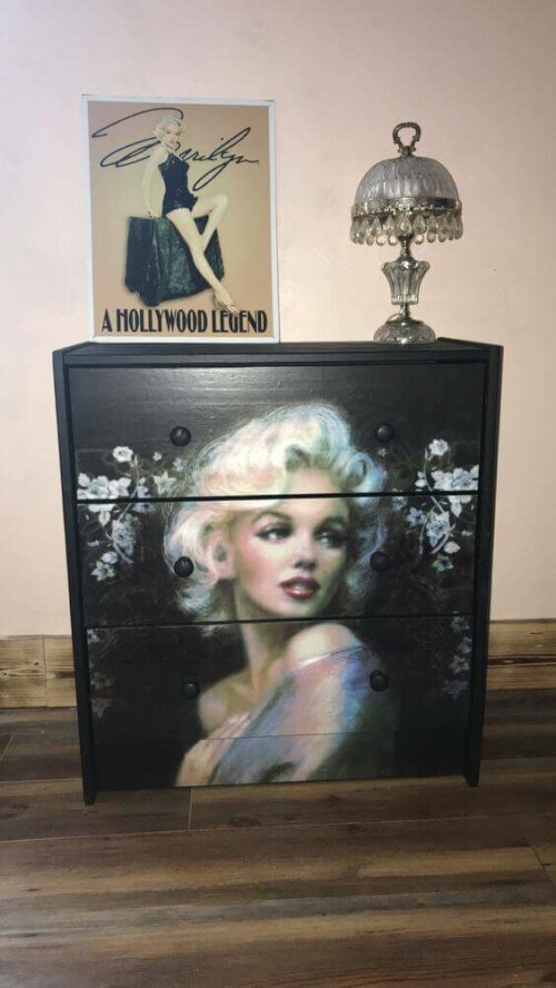 A dresser and a painting of some celebrities.