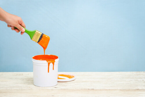 A person taking a brush out of a bucket of orange paint.